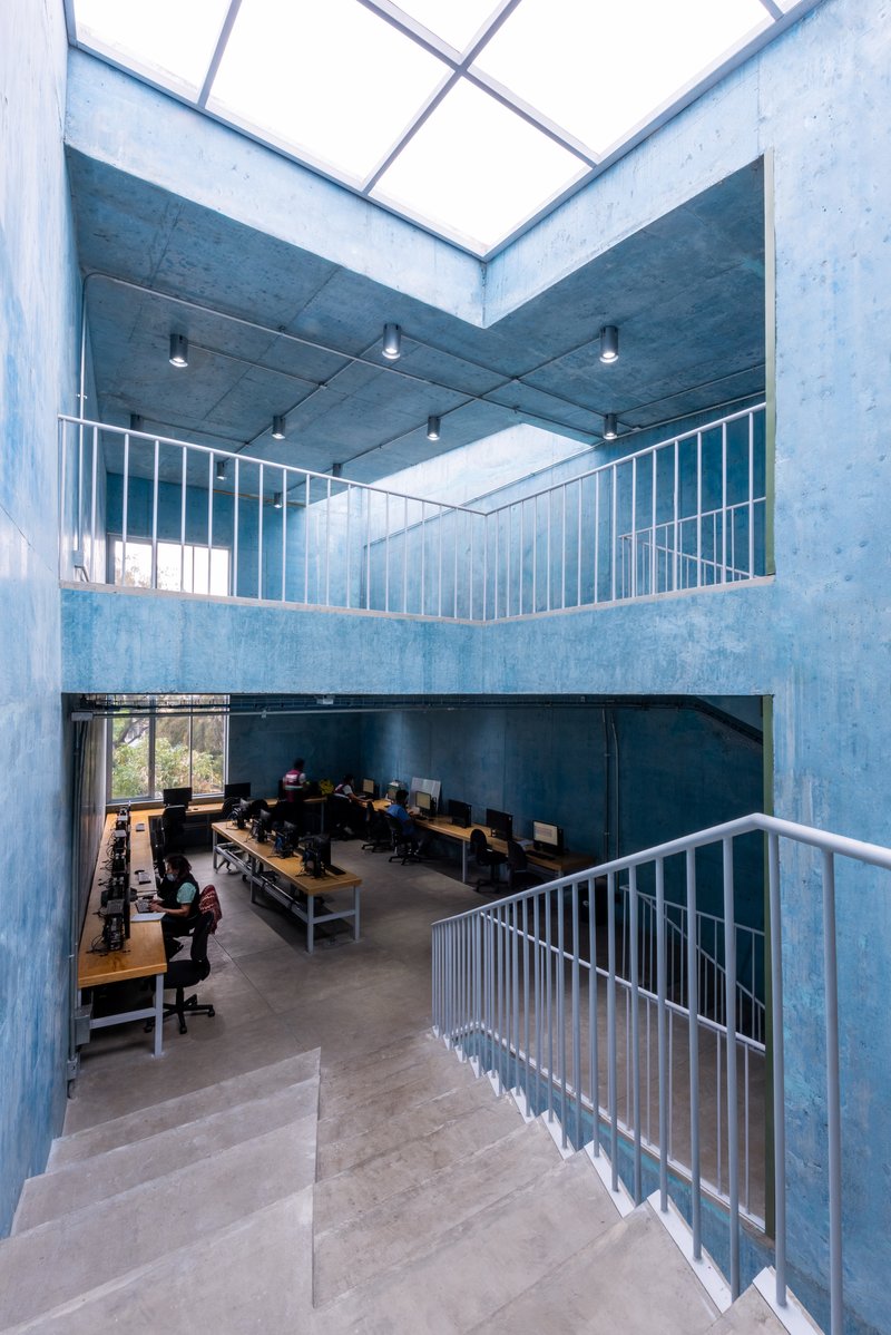 View down the concrete stairwell showing computer workstations on the floor below and a geometric skylight above