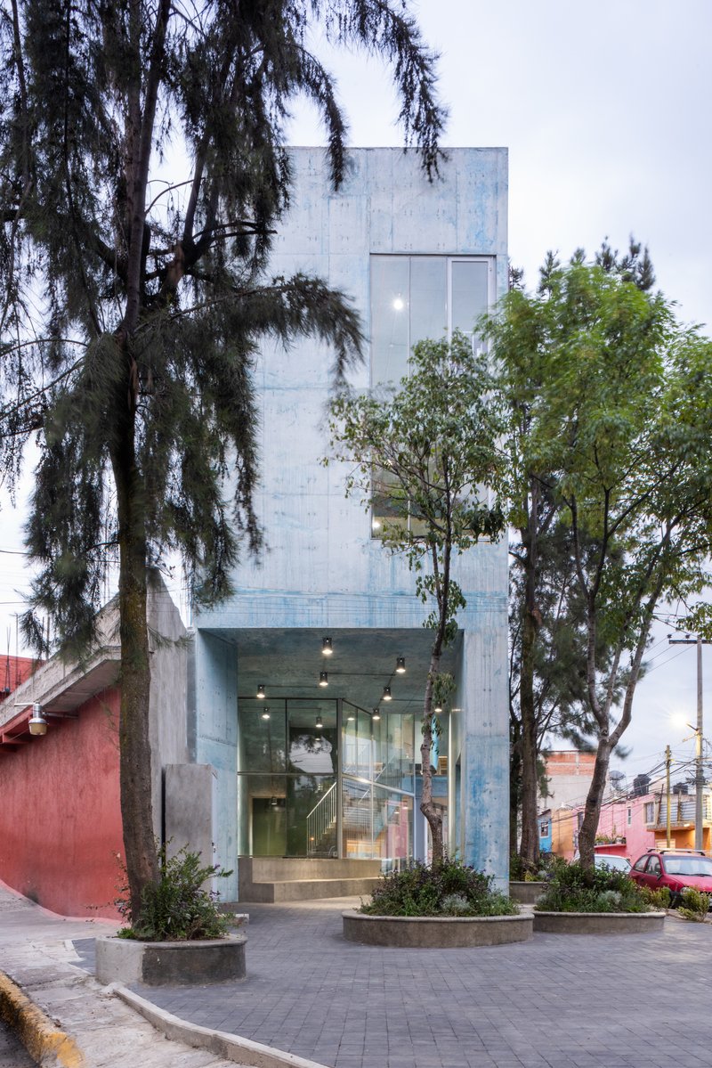 Street facade of the concrete tower framed by mature trees and circular planters at dusk