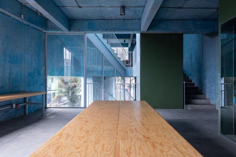 Interior space with plywood work table, interconnecting staircases and glass partitions revealing greenery outside