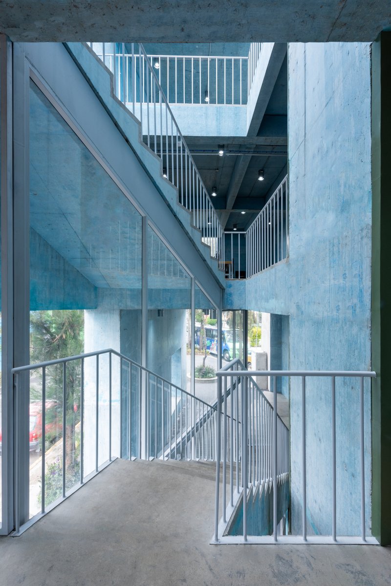 Stairwell corner with metal railing and full-height glazing framing street views through concrete walls