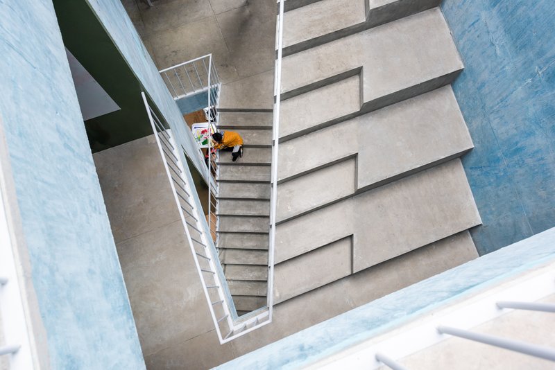 Overhead view of concrete staircase with white metal railings and a person in orange descending