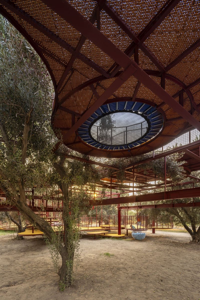 Underside of perforated metal canopy with circular opening and olive trees at dusk