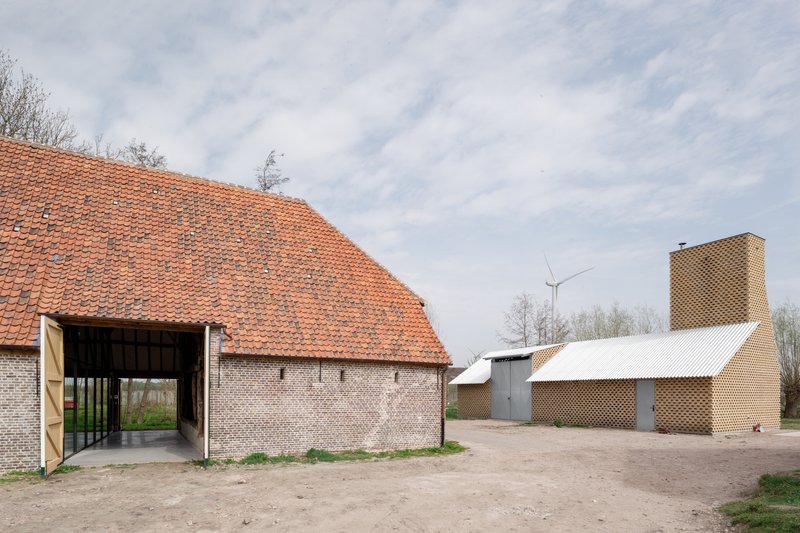 Courtyard view showing brick barn with orange tile roof and perforated brick tower with wind turbine beyond