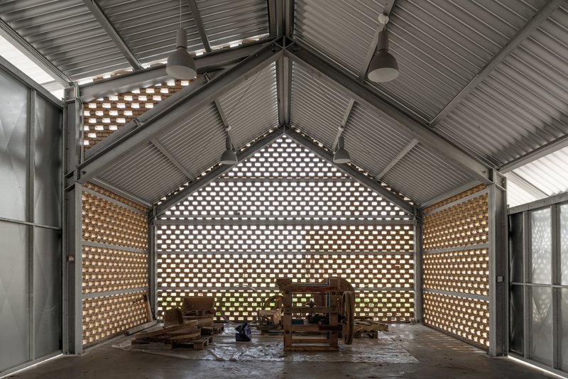 Interior workshop space with perforated brick walls filtering daylight through corrugated metal ceiling