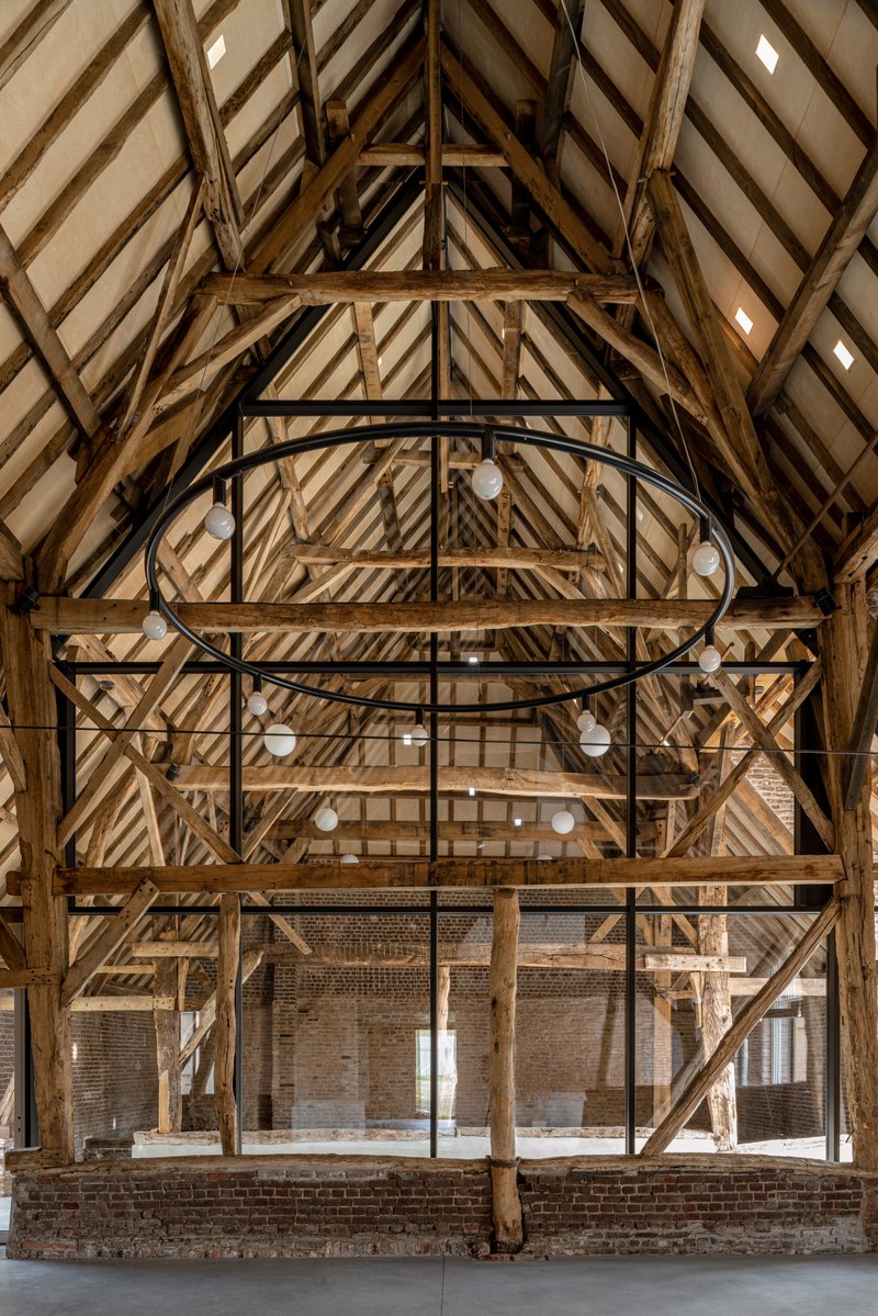 Exposed timber roof trusses and bracing with black steel circular walkway in renovated barn interior