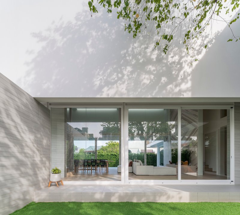 Glass corner facade with dappled tree shadows on white walls and lawn in foreground