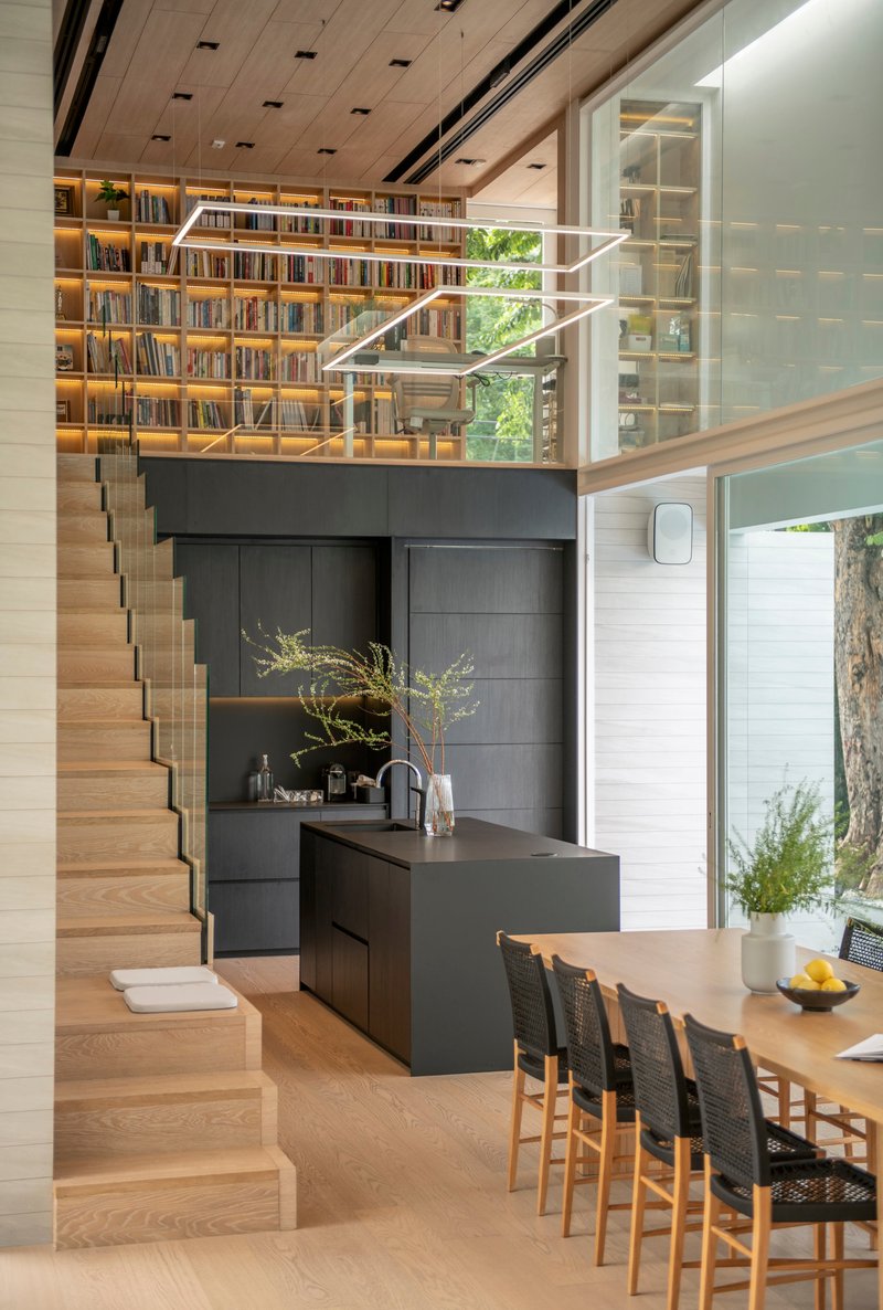 Double-height interior showing timber staircase ascending to mezzanine library above black kitchen island