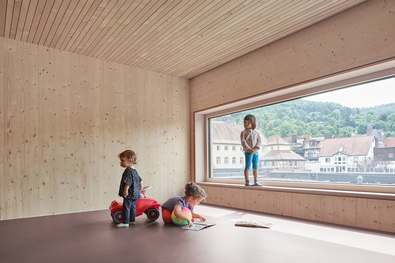Interior room with exposed timber walls and horizontal window framing a village roofscape