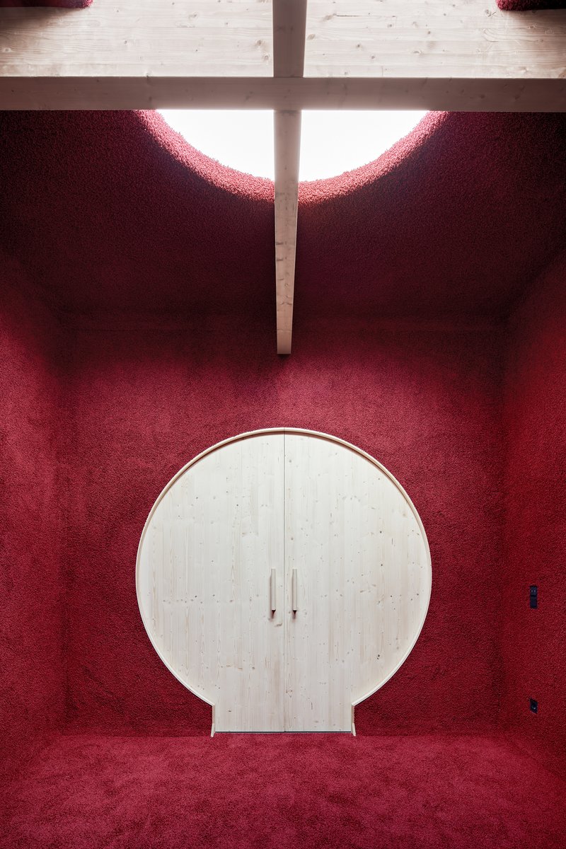 Circular plywood cabinet against deep red carpeted walls beneath a clerestory cross
