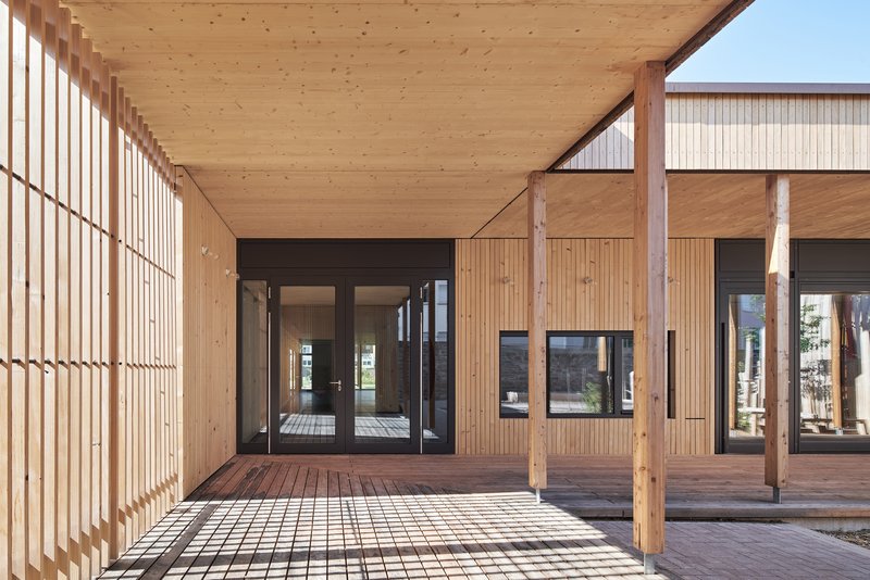 Covered walkway with timber slatted screen wall and exposed plank ceiling creating dappled shadows