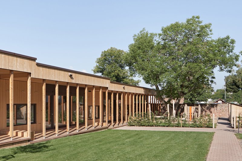 Long elevation showing repeated timber columns along glazed facade with lawn and mature tree canopy
