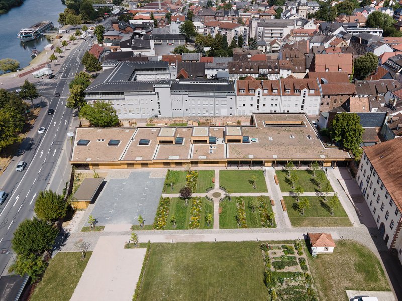 Aerial view of flat timber roof with skylights overlooking geometric courtyard garden and surrounding town