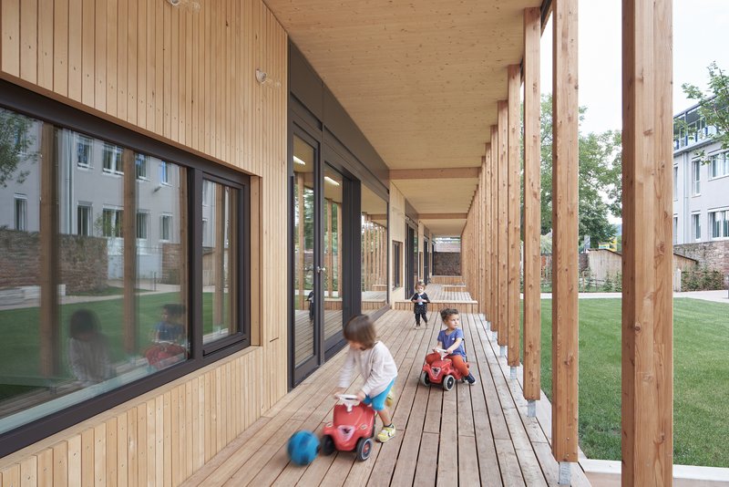 Covered timber walkway with exposed columns and decking where children play with toy cars