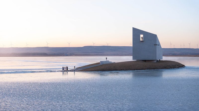 White cubic volume with square window on artificial mound surrounded by ice and visitors at dusk