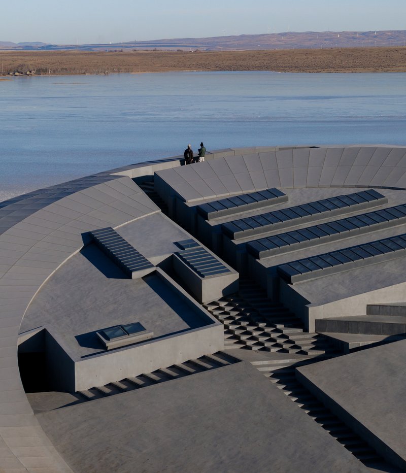 Concrete terraced roof with skylights and two figures standing at the highest platform overlooking the lake