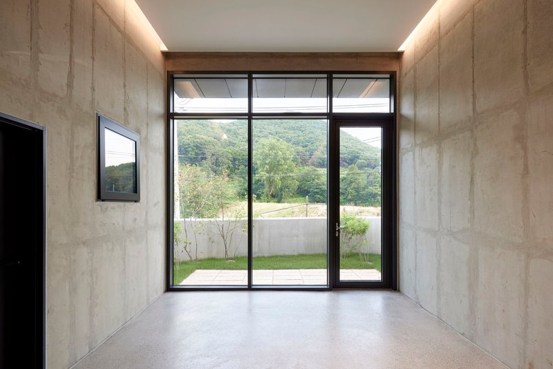 Entry vestibule with board-formed concrete walls and full-height glazed door framing hillside view beyond courtyard