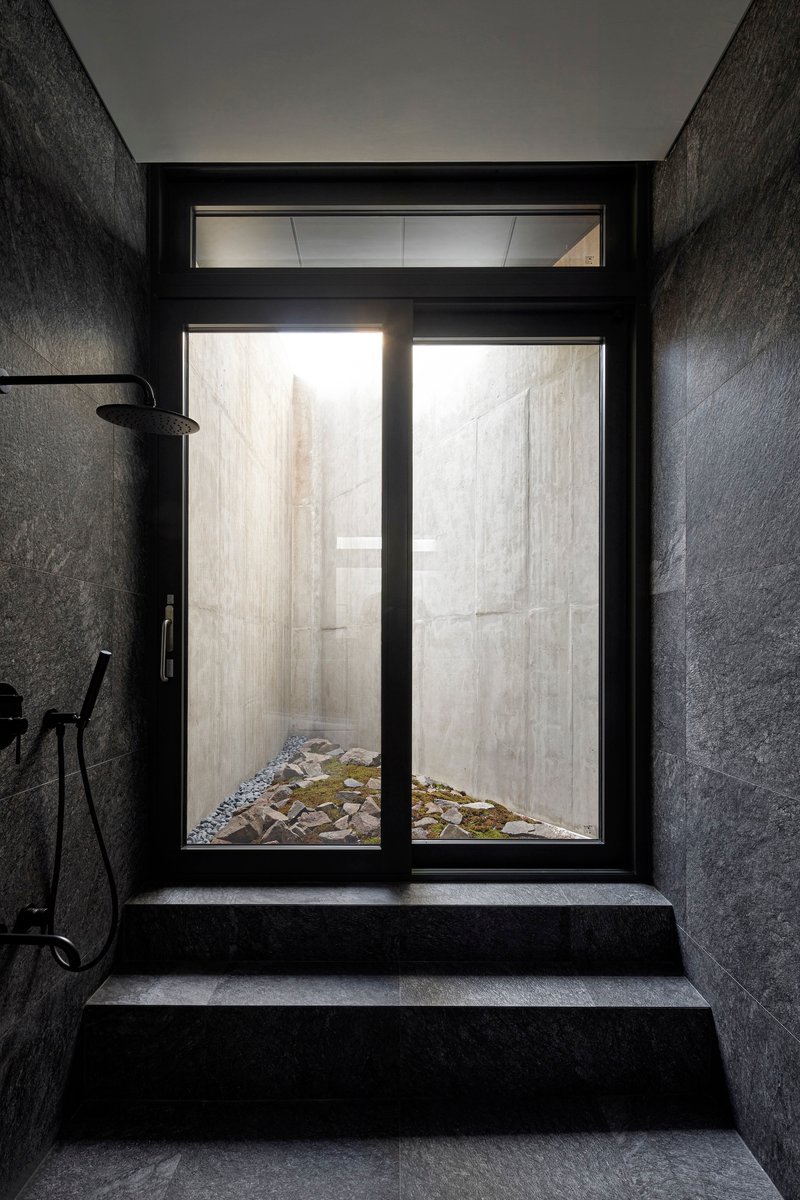 Dark stone shower room with glazed door opening onto a planted courtyard with rocks and moss