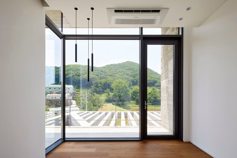 Interior room with timber floor and black-framed glazing overlooking a slatted deck and forested hillside