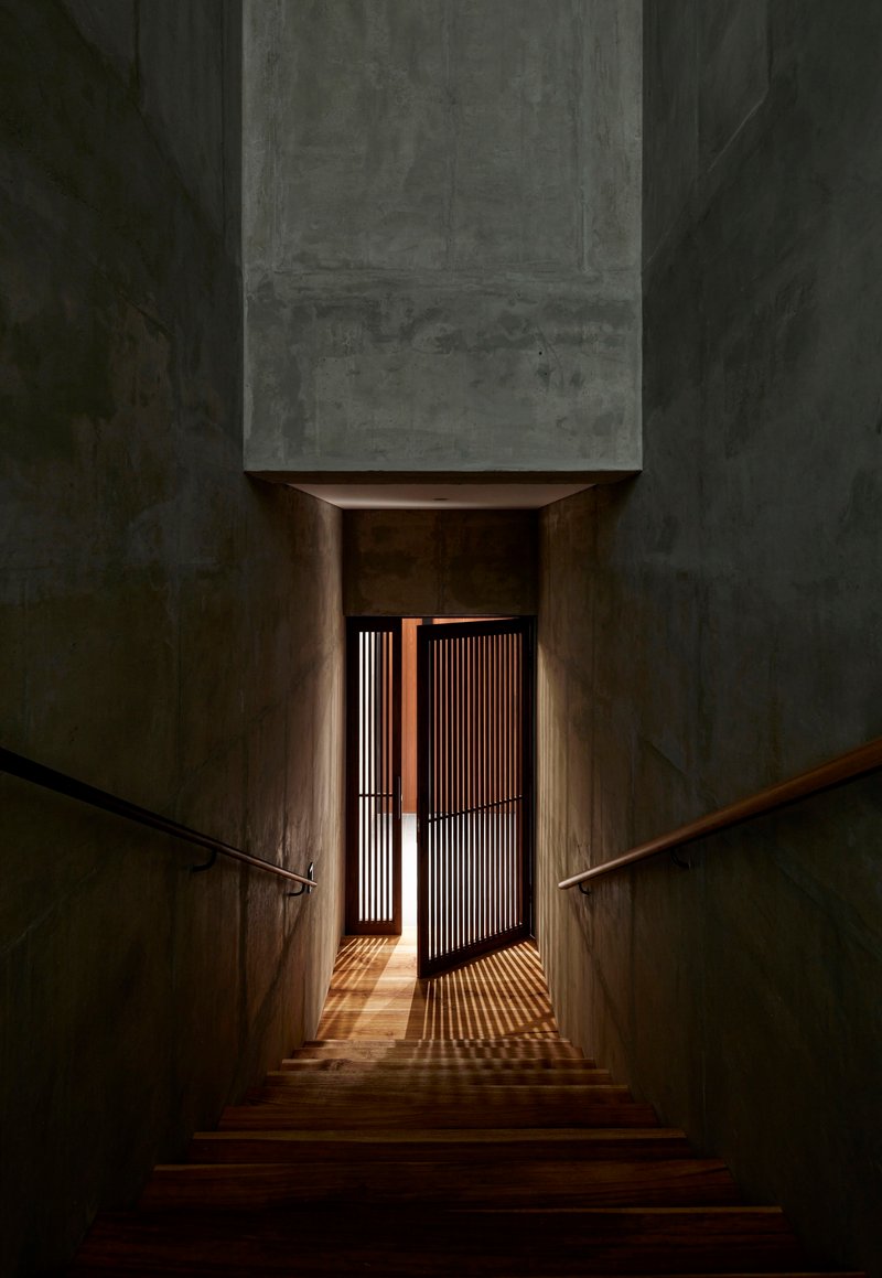 Interior staircase descending toward timber slat door with light filtering through at dusk