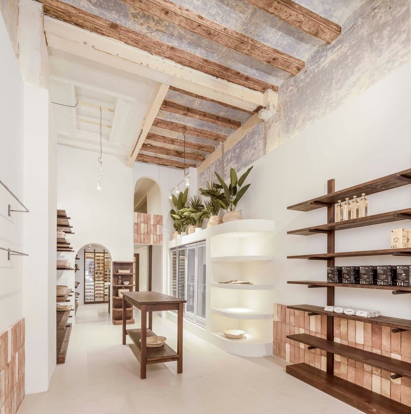 Interior retail space with exposed timber ceiling beams, white plaster walls and wooden shelving displaying products