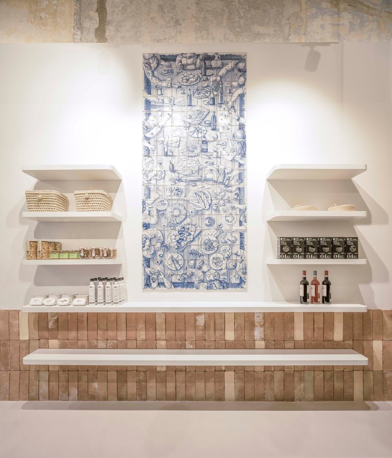 Display wall with blue and white ceramic tile panel above white shelves and terracotta brick base