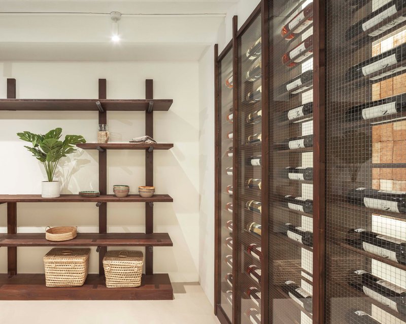 Wine storage alcove with dark timber and wire mesh rack beside open wooden shelving with potted plant