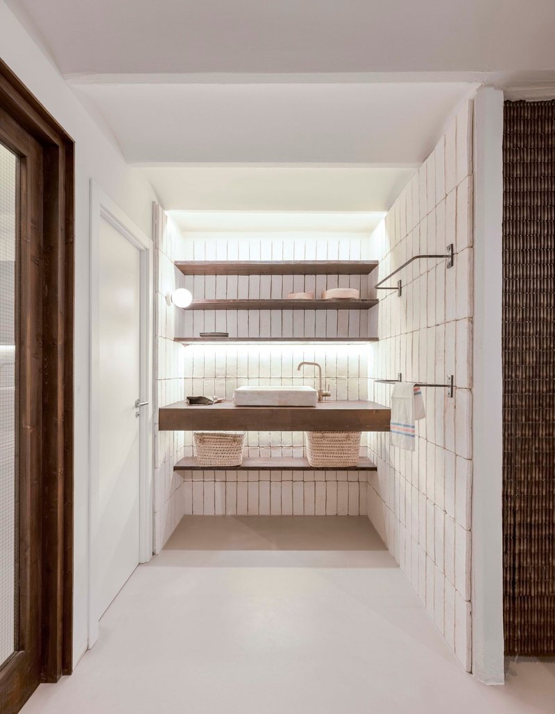 Bathroom with vertical white tile walls and timber floating shelves beneath a skylight