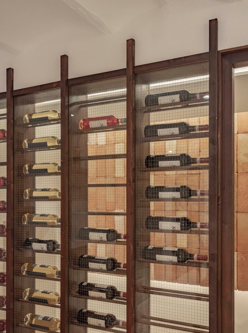 Close-up of wine bottles displayed horizontally on metal pegs within timber and mesh screen
