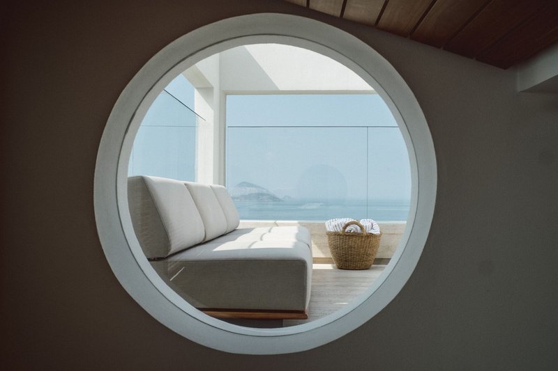 Circular window framing a terrace with daybed and ocean vista beyond