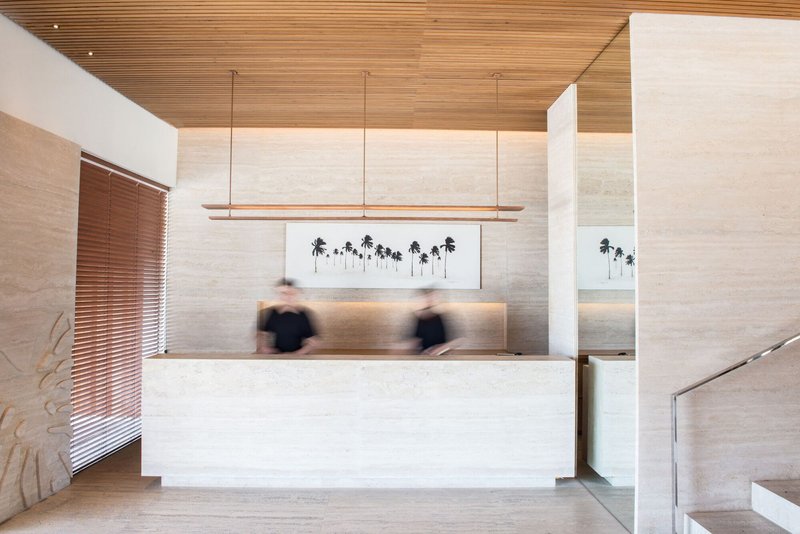 Reception desk with horizontal timber ceiling and blurred figures beneath linear pendant lighting