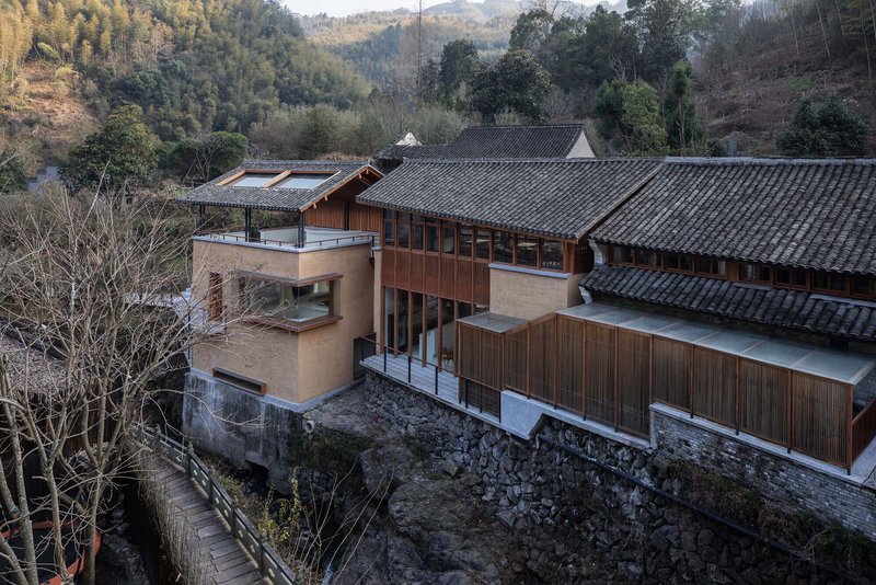 Elevated view showing timber and stucco volumes atop a stone retaining wall among bare trees