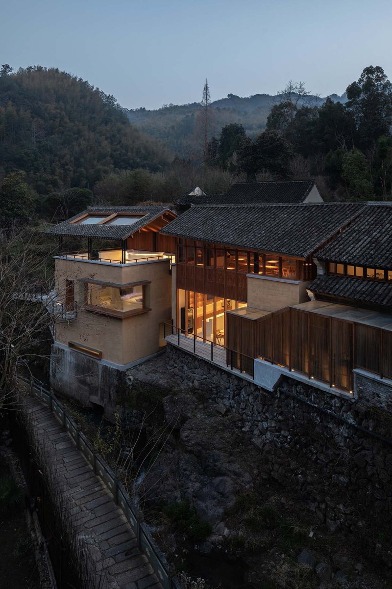 Elevated view of the rammed earth and timber volumes with tiled roofs nestled among neighboring structures at dusk