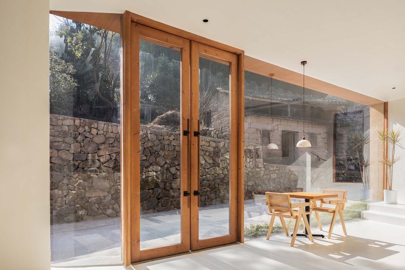 Timber-framed glazed doors opening to a courtyard with stone walls in bright daylight