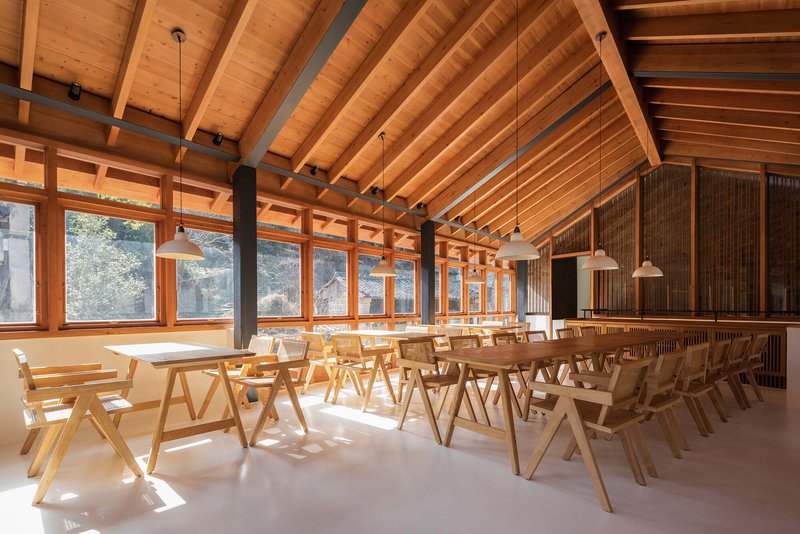 Dining hall with exposed timber rafters, continuous glazing, and rows of timber chairs