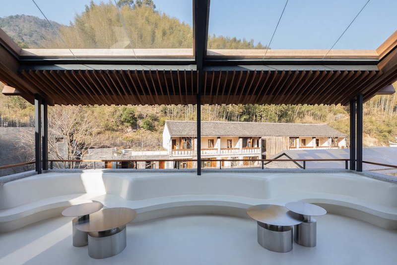 Curved white seating alcove under slatted timber canopy with village rooftops visible beyond