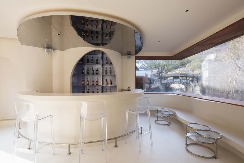 Curved bar with arched display niche and transparent acrylic chairs overlooking a hillside through glazed window