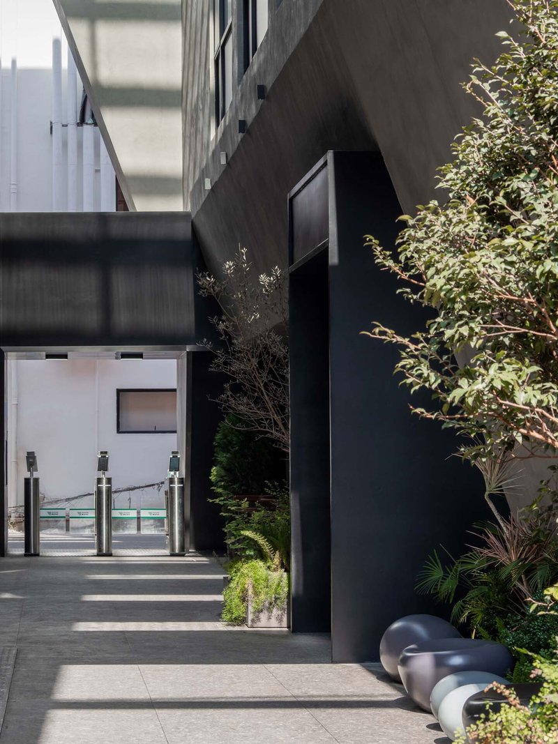 Courtyard entrance with black bollards, planted beds and a glazed security gate in midday sun