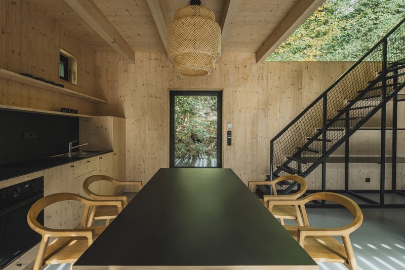 Long dining table with bentwood chairs beneath woven pendant facing doorway to exterior