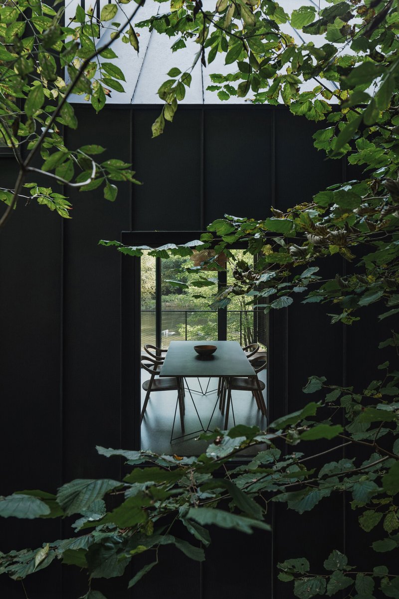 View through tree branches toward a dining area framed by black metal panels
