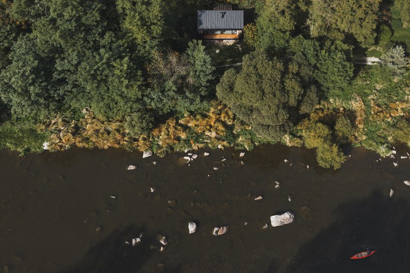 Aerial view of the timber cabin cantilevered above a rocky shoreline with kayaker below