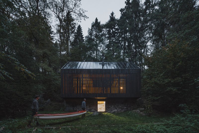 Slatted timber facade glowing with interior light at dusk beside a beached boat