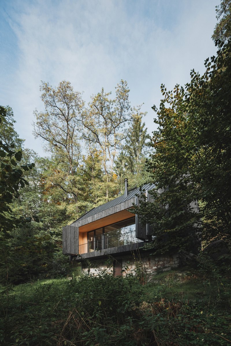 Elevated timber volume on stone base nestled among deciduous trees in dappled daylight