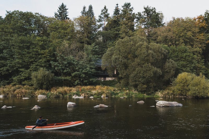 Distant view from the river showing the structure nestled among dense trees with a kayak
