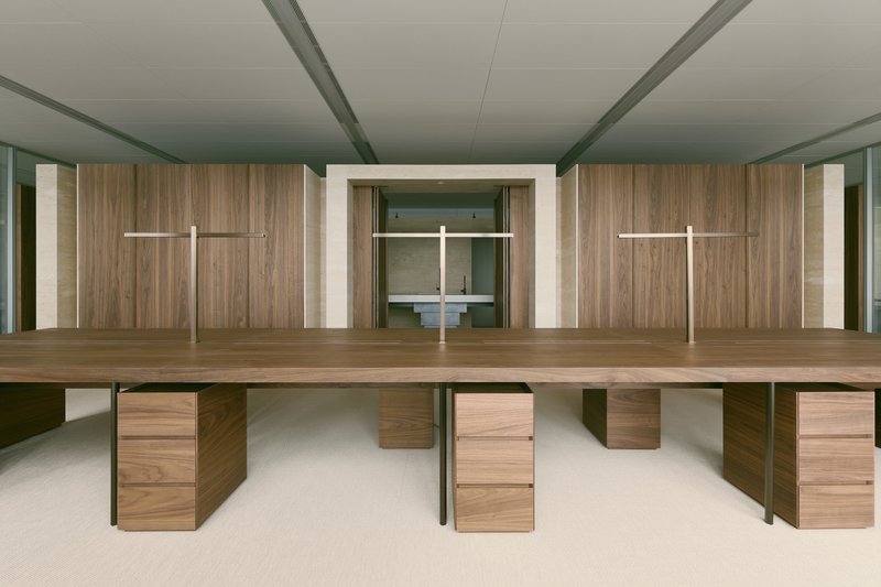 Long workspace with walnut desks and steel legs beneath a timber-clad wall with recessed lighting