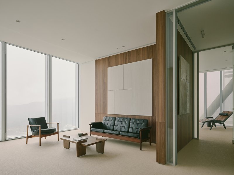 Seating area with walnut wall panel, white ceiling-mounted storage, and glazed partition to adjacent room