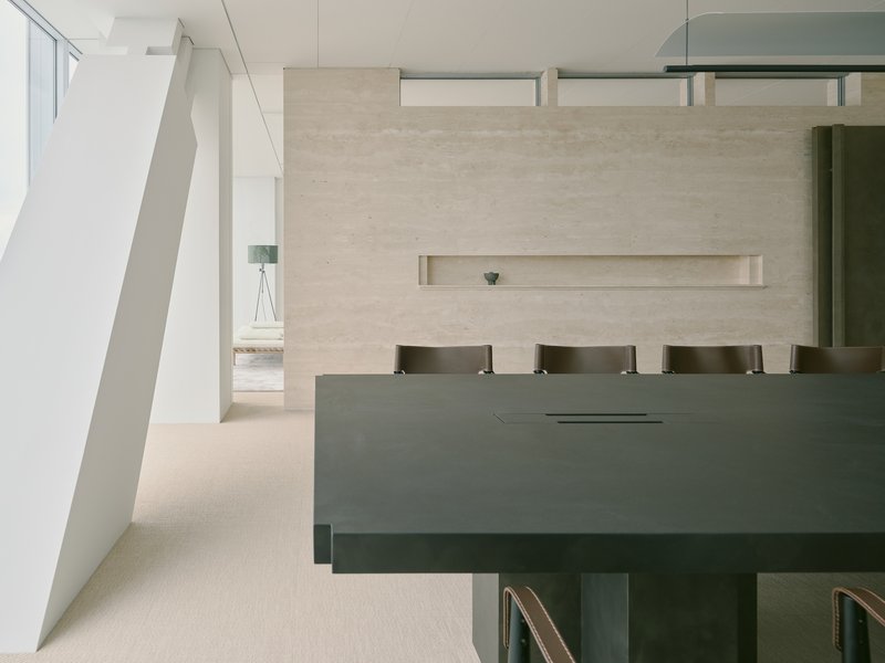 Reception desk in grey metal beneath a textured plaster wall with horizontal recessed niche