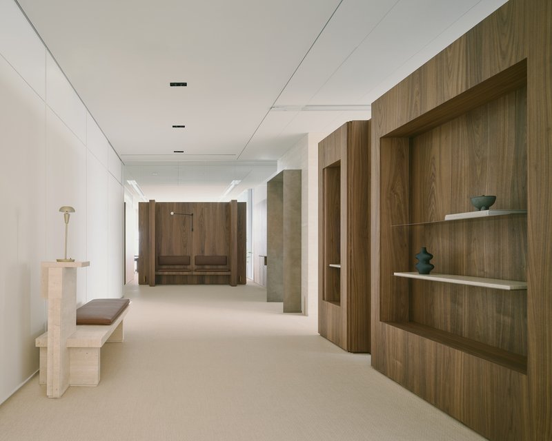 Corridor with walnut display niches and stone bench leading to built-in seating booth at end