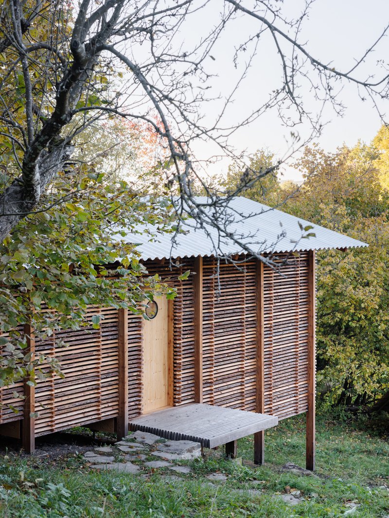 Corner of the horizontal slat facade with corrugated metal roof and outdoor bench under bare branches