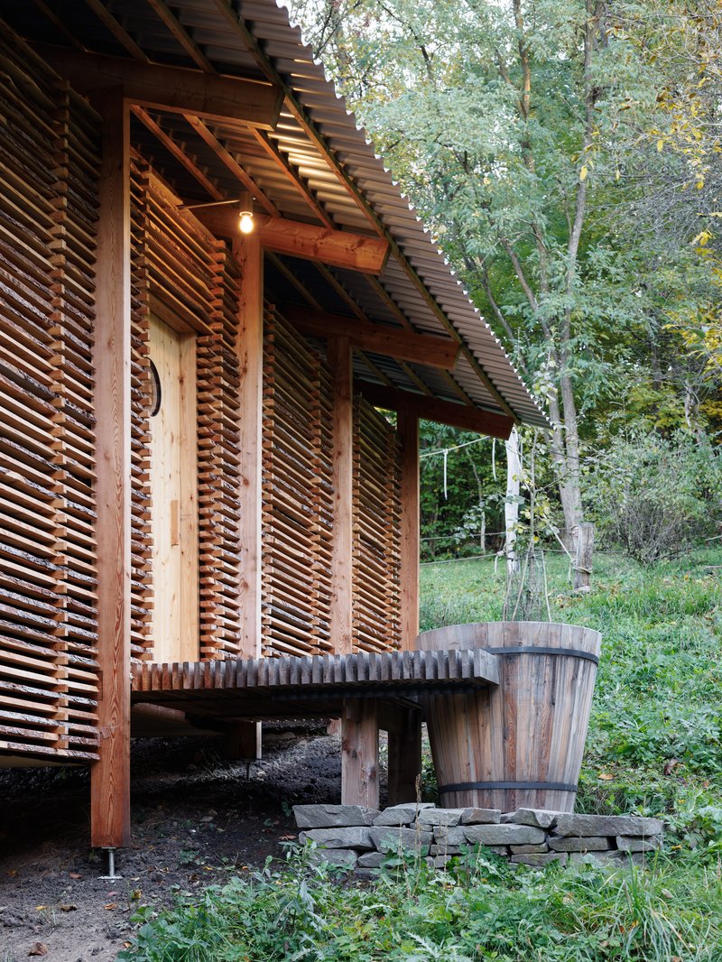 Corner detail showing timber column, horizontal slat wall, and wooden barrel beside low deck at dusk