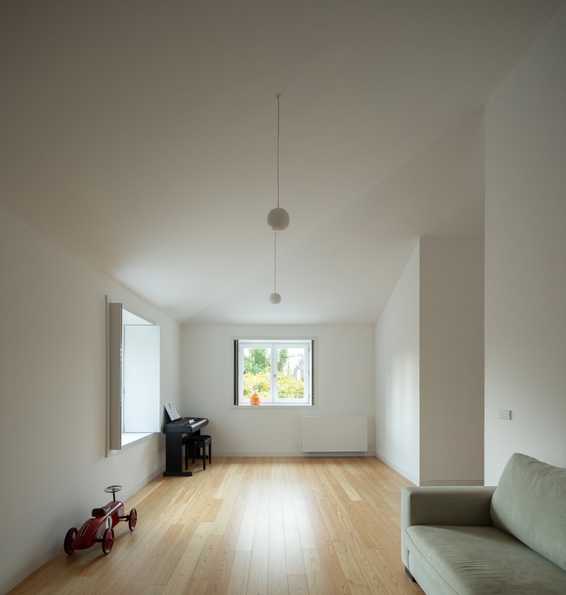 White-walled living room with vaulted ceiling, pendant lights, and a framed window overlooking greenery